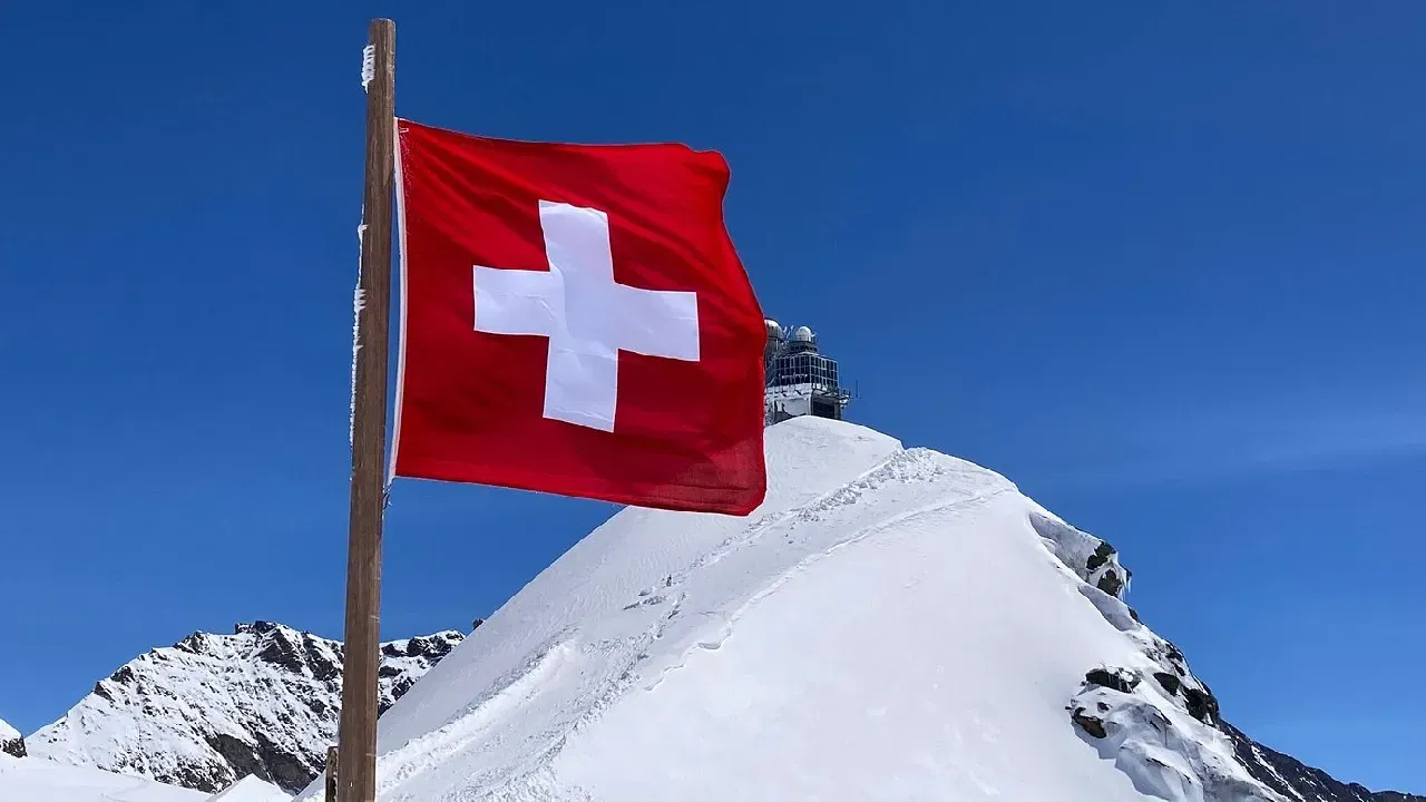 Swiss flag waving in-front of Alpine ranges in Jungfraujoch 