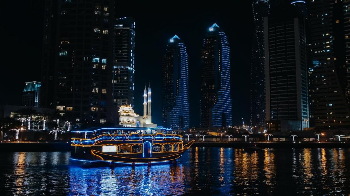 Illuminated dhow cruise boat sailing through Dubai Marina at night, showcasing popular cruise routes.