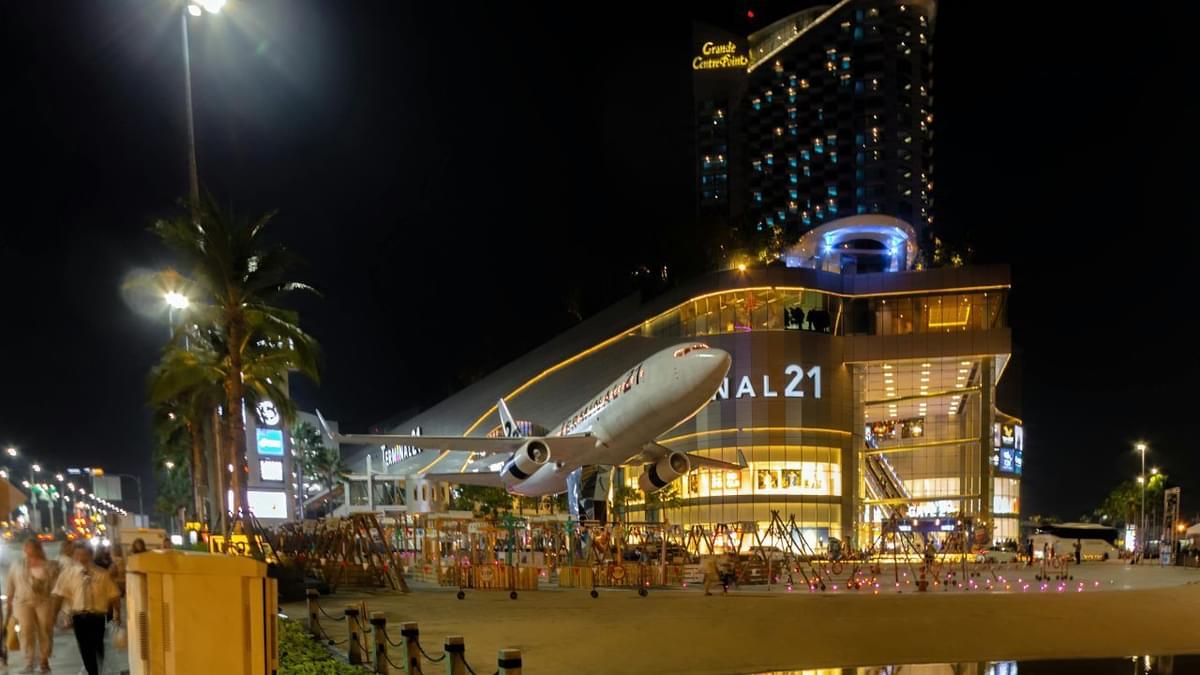 Night view of Terminal 21 shopping mall in Pattaya, Thailand, featuring a large airplane installation and illuminated modern architecture.