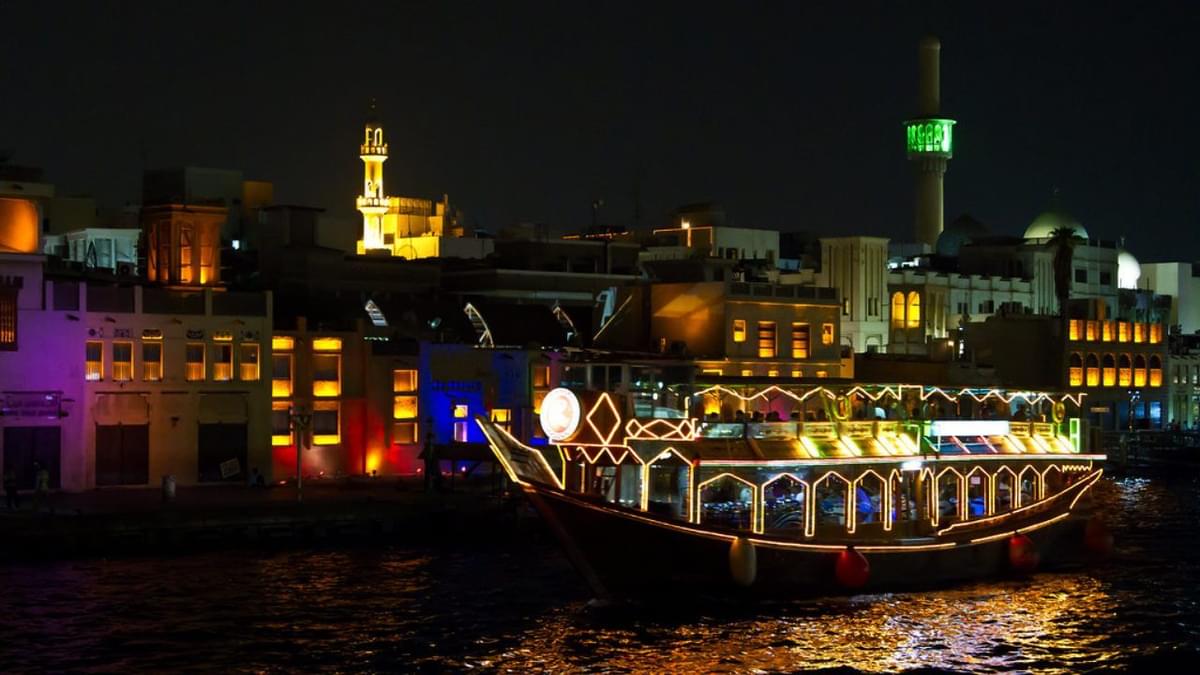 Colorfully lit dhow cruise boat with guests enjoying evening views along Dubai Creek’s historic skyline.